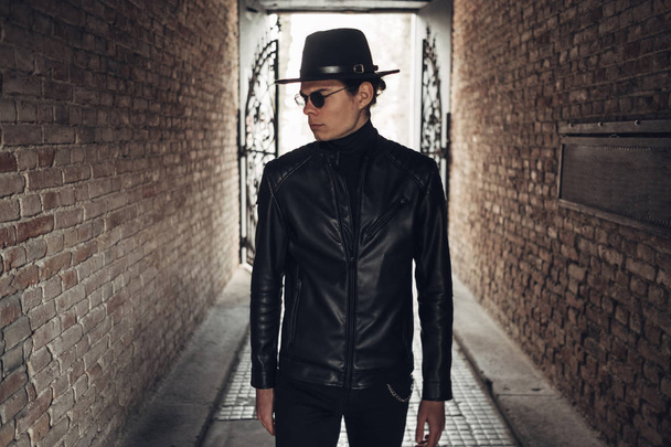 Portret van stijlvolle jonge man in zwart lederen jas en hoed - Foto, afbeelding