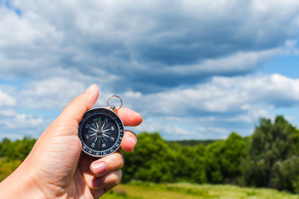 компас в руке крупным планом на фоне летнего пейзажа
 - Фото, изображение