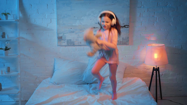 podekscytowany dziecko w słuchawkach tańczyć na łóżku w nocy - Materiał filmowy, wideo