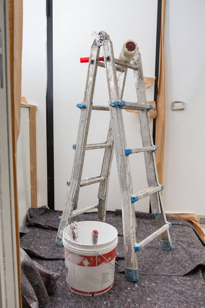 Escalera y herramientas para la pintura y el suelo cubierto con láminas protectoras
 - Foto, Imagen