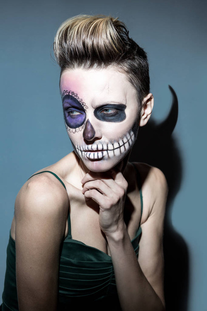 Halloween. Beautiful woman with bright black halloween makeup , hairstyle and shadow with horns isolated over dark gray background - Foto, Imagem