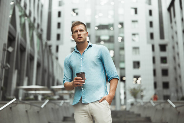 young handsome man holding cup of coffee walking down the street near business center - 写真・画像