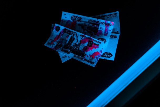 blue ultraviolet lightning on russian money on black  - Photo, Image