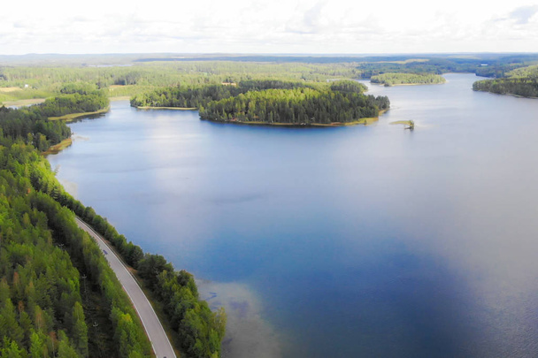Εναέρια θέα της λίμνης με το νησί, το δρόμο και το δάσος σε μια καλοκαιρινή ηλιόλουστη μέρα στη Φινλανδία. Φωτογράφιση με κηφήνες - Φωτογραφία, εικόνα