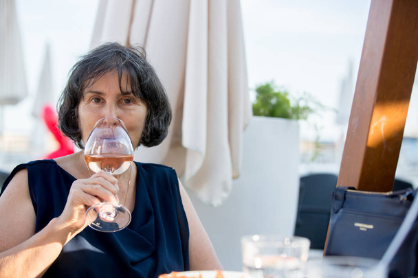 Elderly woman, drinking glass of rose wine on the beach  - Foto, immagini