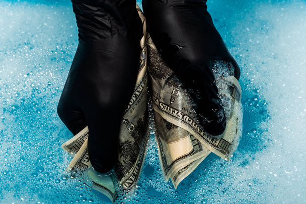 vista recortada del hombre en guantes de goma negro lavado de billetes de dólar
  - Foto, Imagen