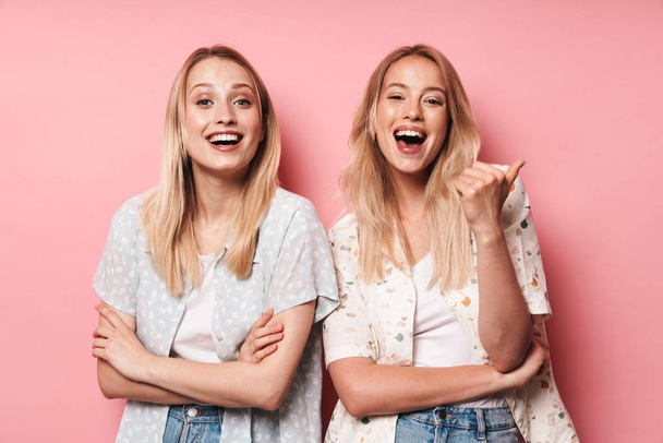 Happy smiling pretty blondes women friends posing isolated over pink wall background showing thumbs up gesture. - Foto, afbeelding