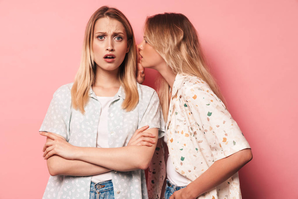 Displeased negative beautiful blondes women friends posing isolated over pink wall background talking with each other gossiping. - Fotografie, Obrázek