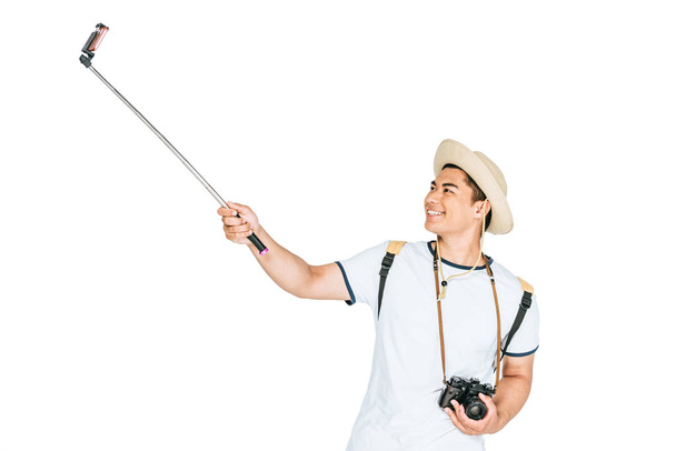 cheerful asian man taking selfie on smartphone with selfie stick isolated on white - Fotoğraf, Görsel