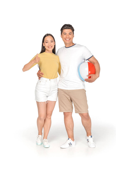 glücklich asiatische Mann hält Strandball und umarmt Freundin zeigt Daumen nach oben auf weißem Hintergrund - Foto, Bild