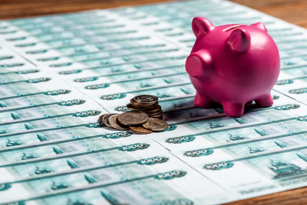 selective focus of pink piggy bank near metallic coins on russian money  - Foto, Bild