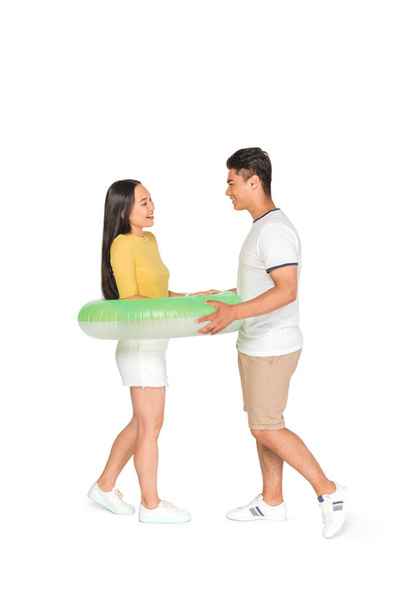 handsome asian man putting swim ring on cheerful girlfriend on white background - Photo, Image