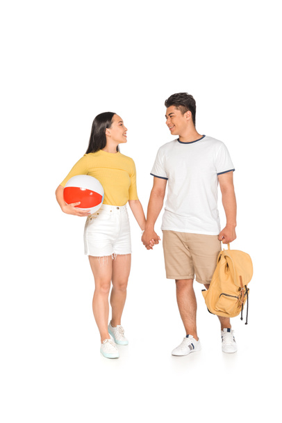 молодий азіатський чоловік з рюкзаком тримає руки з веселою дівчиною з пляжним м'ячем на білому тлі
 - Фото, зображення