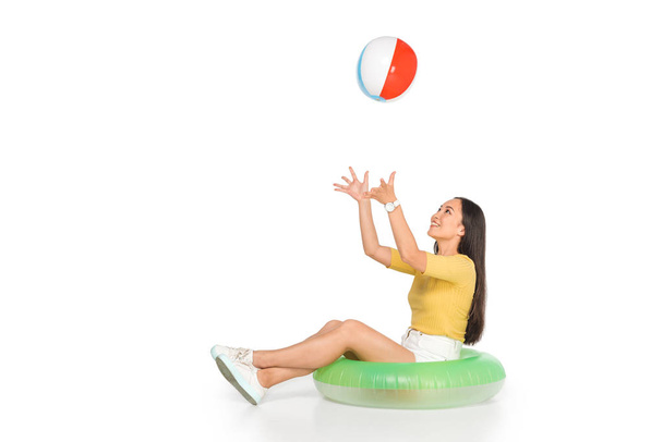 fiatal ázsiai nő ül úszni gyűrűt, és játék strandröplabda fehér alapon - Fotó, kép