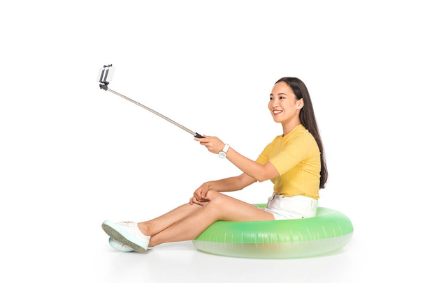 attractive asian woman taking selfie on smartphone with selfie stick on white background - Valokuva, kuva