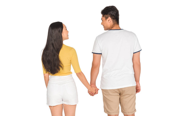 back view of young couple in summer clothing holding hands on white background - 写真・画像