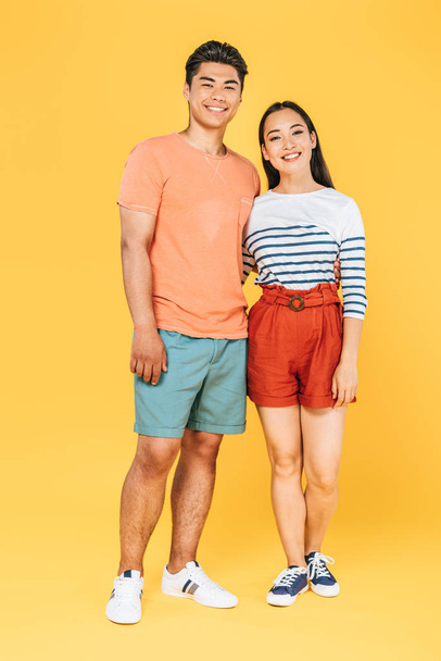 fröhliches asiatisches Paar in Sommerkleidung blickt in die Kamera auf gelbem Hintergrund - Foto, Bild