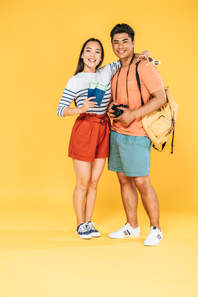 gai asiatique fille tenant passeports et billets d'avion tout en étreignant heureux petit ami sur fond jaune
 - Photo, image