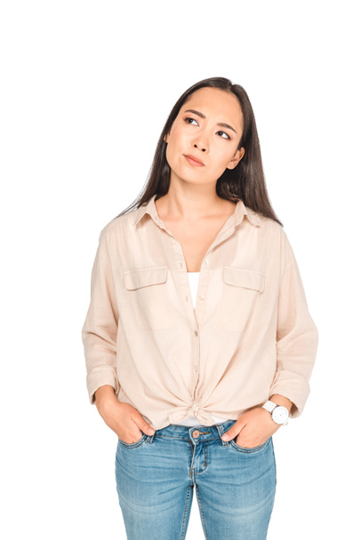 thoughtful asian woman holding hands in pockets while looking away isolated on white - Φωτογραφία, εικόνα