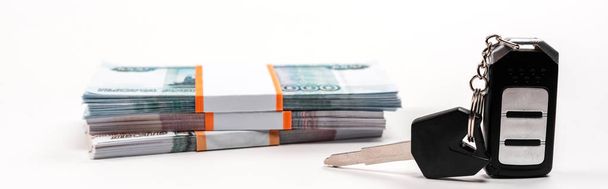 panoramic shot of car key with key chain near stacks of russian money on white  - Fotoğraf, Görsel