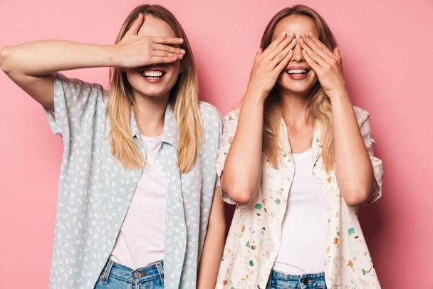 Cheerful girls women friends sisters isolated over pink wall background covering eyes. - Foto, Imagem