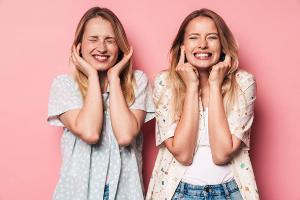 Displeased girls women friends sisters isolated over pink wall background covering ears because of loud. - Fotoğraf, Görsel