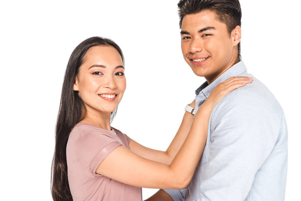 glückliche asiatische Frau hält die Hände auf den Schultern ihres lächelnden Freundes, während sie isoliert auf weiß in die Kamera schaut - Foto, Bild