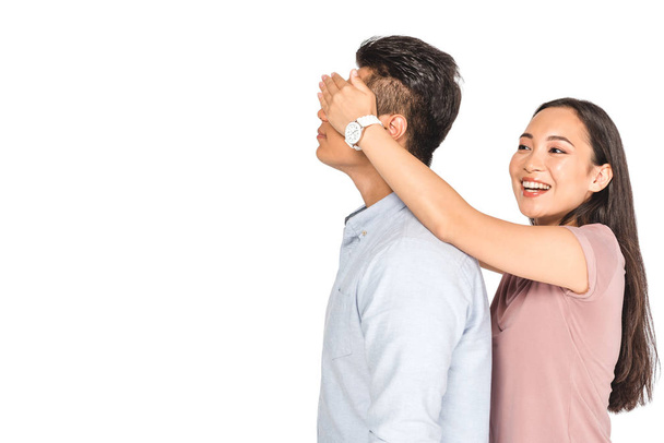 cheerful asian girl closing eyes of boyfriend with hands isolated on white - Φωτογραφία, εικόνα