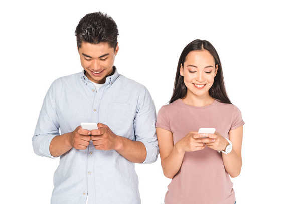 young asian couple smiling while using smartphones isolated on white - Fotoğraf, Görsel
