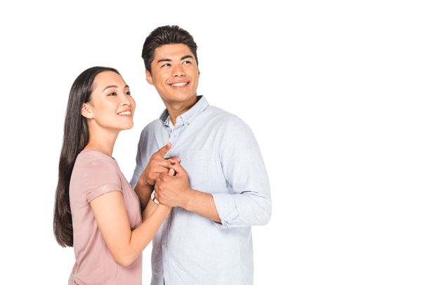 happy asian couple holding hands while smiling and looking away isolated on white - Фото, изображение