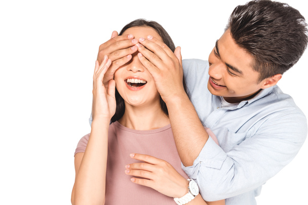 handsome asian man closing eyes of cheerful girlfriend with hands isolated on white - Fotografie, Obrázek