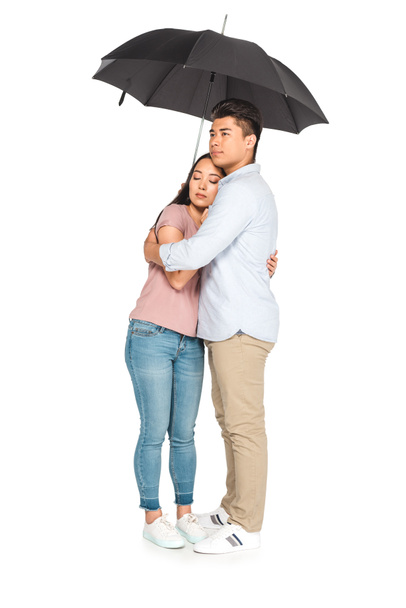 handsome asian man hugging pretty girlfriend while standing under umbrella on white background - Foto, imagen