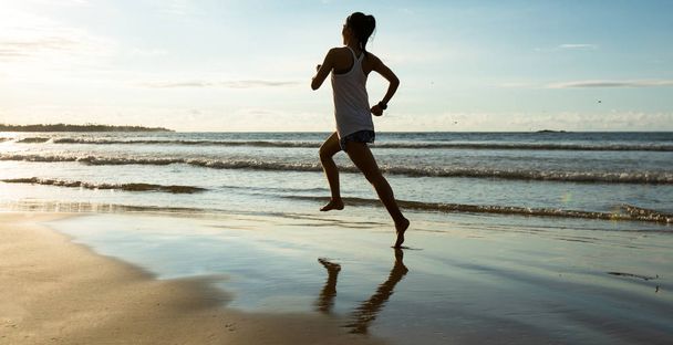 Fitness woman runner running on sunrise beach - 写真・画像
