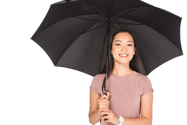pretty asian girl holding black umbrella and smiling at camera isolated on white - Zdjęcie, obraz