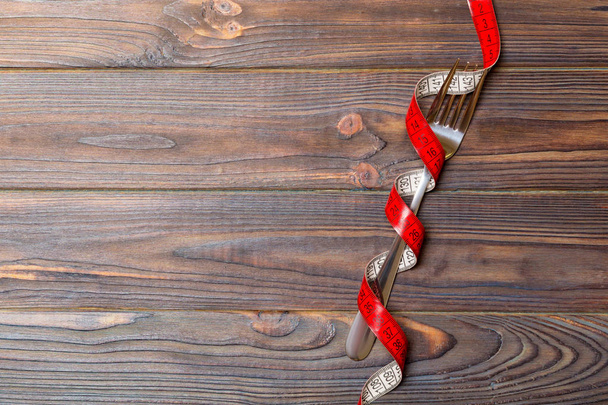 Composición de cinta métrica envuelta en rizos y tenedor sobre fondo de madera con espacio vacío para su diseño. Concepto de sobrepeso
 - Foto, imagen