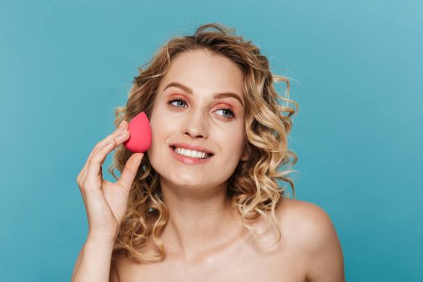 Image of pleased half-naked woman applying makeup with sponge - Photo, Image