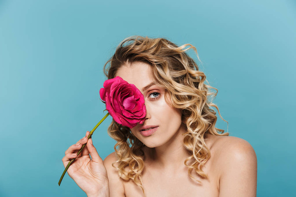 Image of pretty half-naked woman with curly hair looking at camera while holding pink flower - Foto, Bild