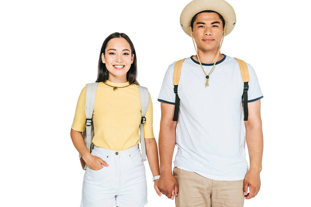 two cheerful asian tourists holding hands and smiling at camera isolated on white - Photo, Image