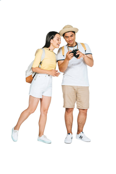 cheerful asian man showing digital camera to smiling girlfriend on white background - 写真・画像