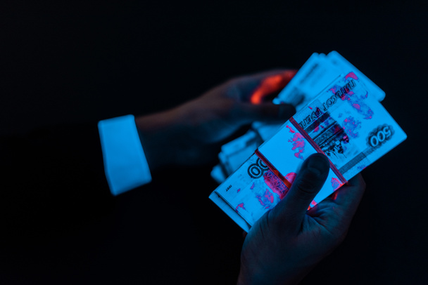 vista ritagliata di uomo in possesso di denaro russo sotto l'illuminazione UV blu isolato su nero
  - Foto, immagini