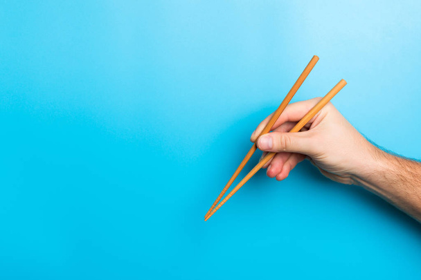 Imagen creativa de palillos de madera en manos masculinas sobre fondo azul. Comida japonesa y china con espacio para copias
 - Foto, Imagen