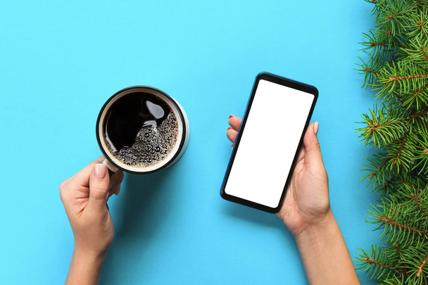Frauenhände mit schwarzem Handy mit weißem Bildschirm und Kaffeebecher. Attrappe mit Kopierraum. Draufsicht auf blauem Hintergrund, flache Lage - Foto, Bild