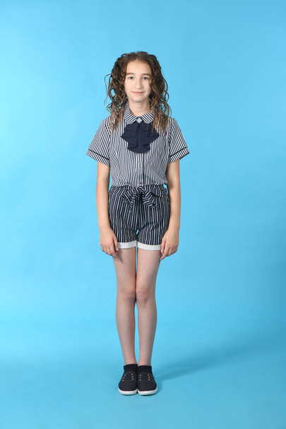 Portrait of adorable smiling schoolgirl with curl hair, standing isolated on a blue background. - Φωτογραφία, εικόνα
