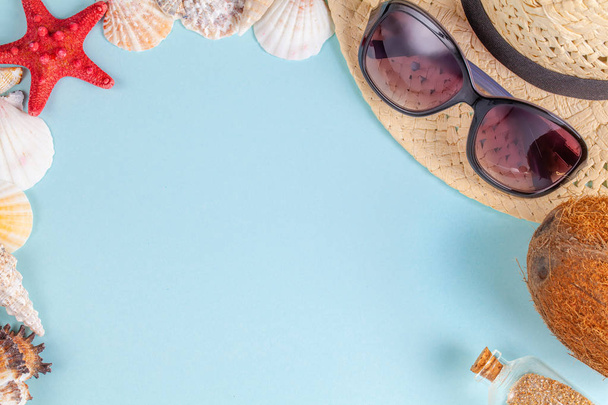 Sunglasses, coconut, starfish, shells, straw hat and bottle with sand on blue background - Zdjęcie, obraz