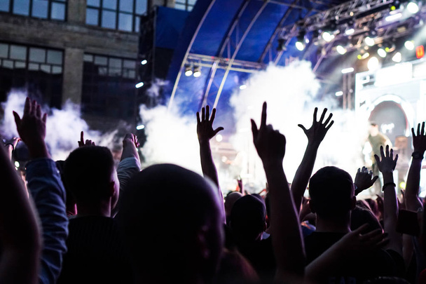 Multitud de conciertos asistiendo a un concierto, las siluetas de la gente son visibles, retroiluminadas por luces de escenario. Las manos levantadas y los teléfonos inteligentes son visibles aquí y allá
. - Foto, imagen