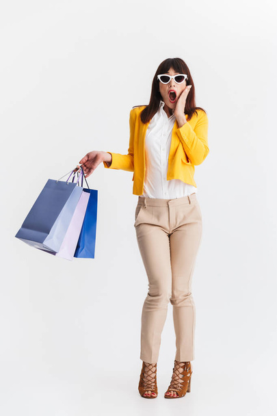 Shocked young business woman posing isolated over white background holding shopping bags. - Foto, Bild