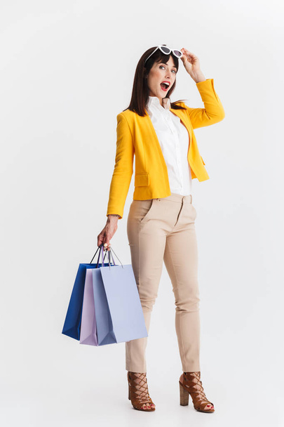 Shocked young business woman posing isolated over white background holding shopping bags. - 写真・画像