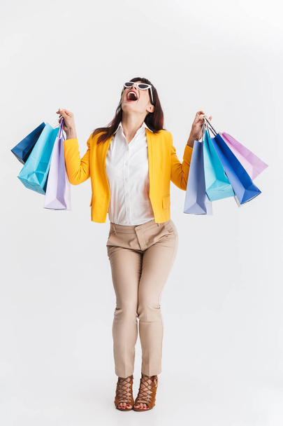 Shocked young business woman posing isolated over white background holding shopping bags. - Φωτογραφία, εικόνα