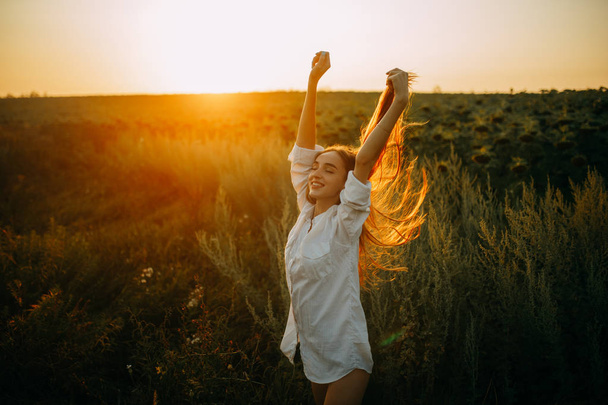 Szczęśliwa radosna kobieta jest chodzenie na łące o zachodzie słońca. - Zdjęcie, obraz