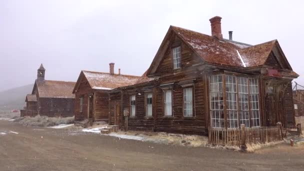 Vervallen houten huizen van het schilderachtige Bodie, Nevada verwering de barre winterse omstandigheden. SnowStorm bedekt langzaam de spookstad en het rustige platteland in een afgelegen deel van de VS. Koele houten gebouwen. - Video